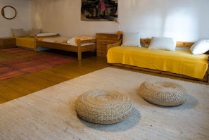 A bedroom with two beds, a wooden dresser, a round woven ottoman, and a colorful rug. - Růžová chalupa u Šimánků (Rtyne v Podkrkonosí)