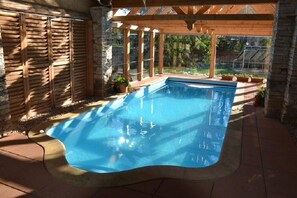 A swimming pool with a wooden deck and stone walls, surrounded by potted plants. - Růžová chalupa u Šimánků (Rtyne v Podkrkonosí)