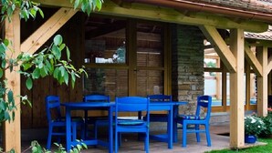 An outdoor wooden deck with a stone wall, blue chairs, and a table. - Růžová chalupa u Šimánků (Rtyne v Podkrkonosí)