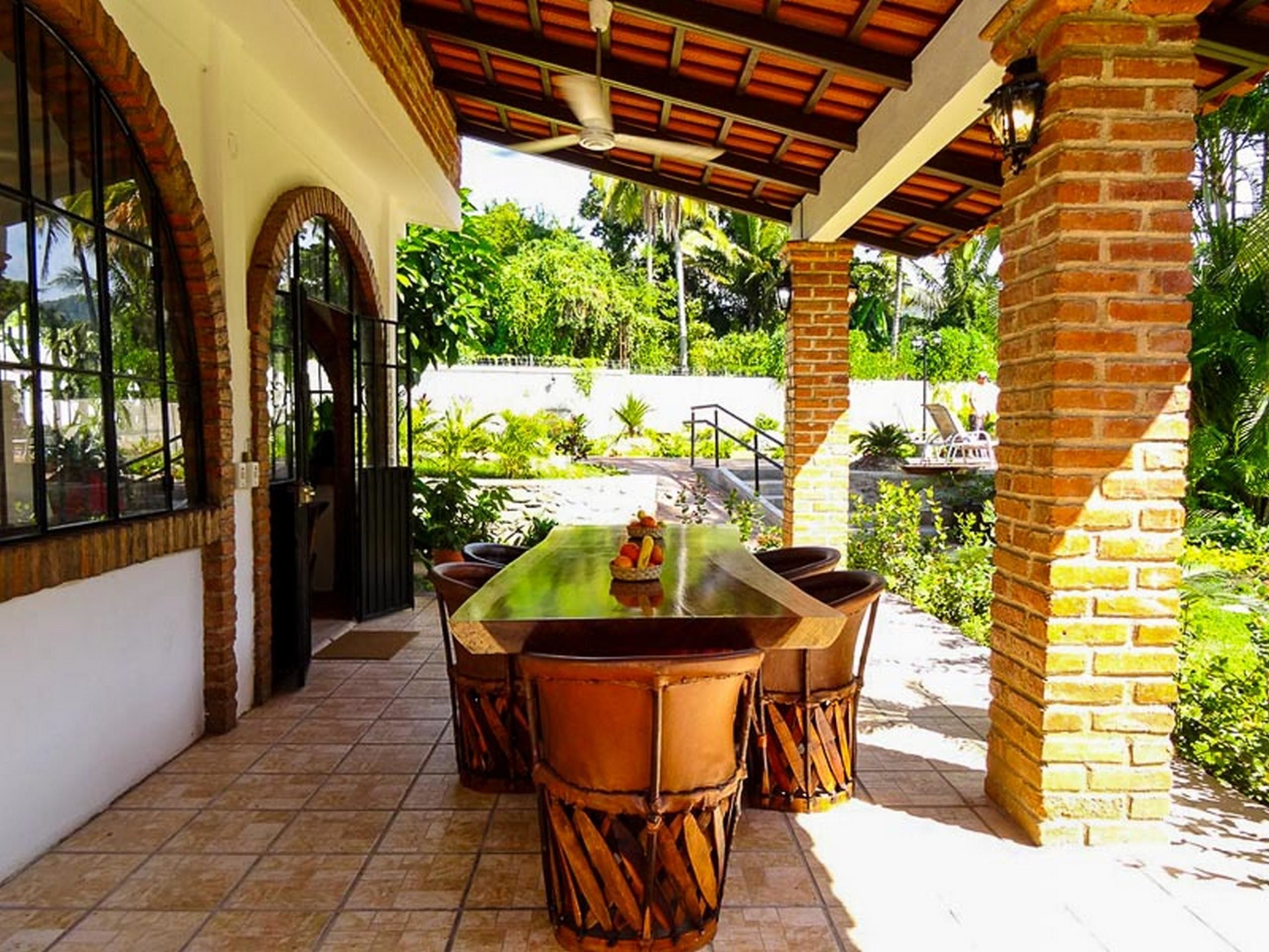An outdoor patio with a table and chairs, surrounded by brick pillars and a covered area with a tiled floor.
