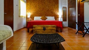 Une chambre à coucher avec une tête de lit en bois à motifs en chevrons, une couvre-lit rouge, une commode en bois et un banc en osier.