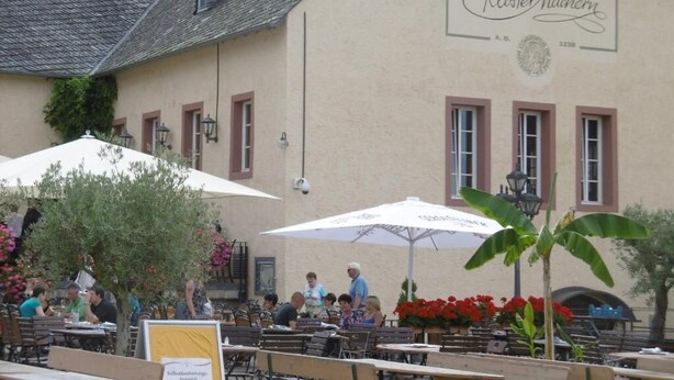Un área de estar al aire libre con mesas y sombrillas frente a un edificio con un letrero que dice "Kloster Machern".