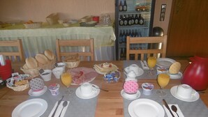 Una mesa de desayuno dispuesta con platos, cubiertos y diversos alimentos, como pan, bollería y bebidas.