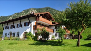 A two-story building with a balcony, surrounded by greenery and mountains in the background. - Gästehaus Gritscher (Schliersee)