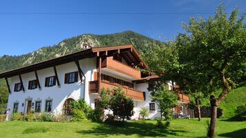 Traditional chalet-style building with a balcony overlooking lush green hills and well-maintained gardens.