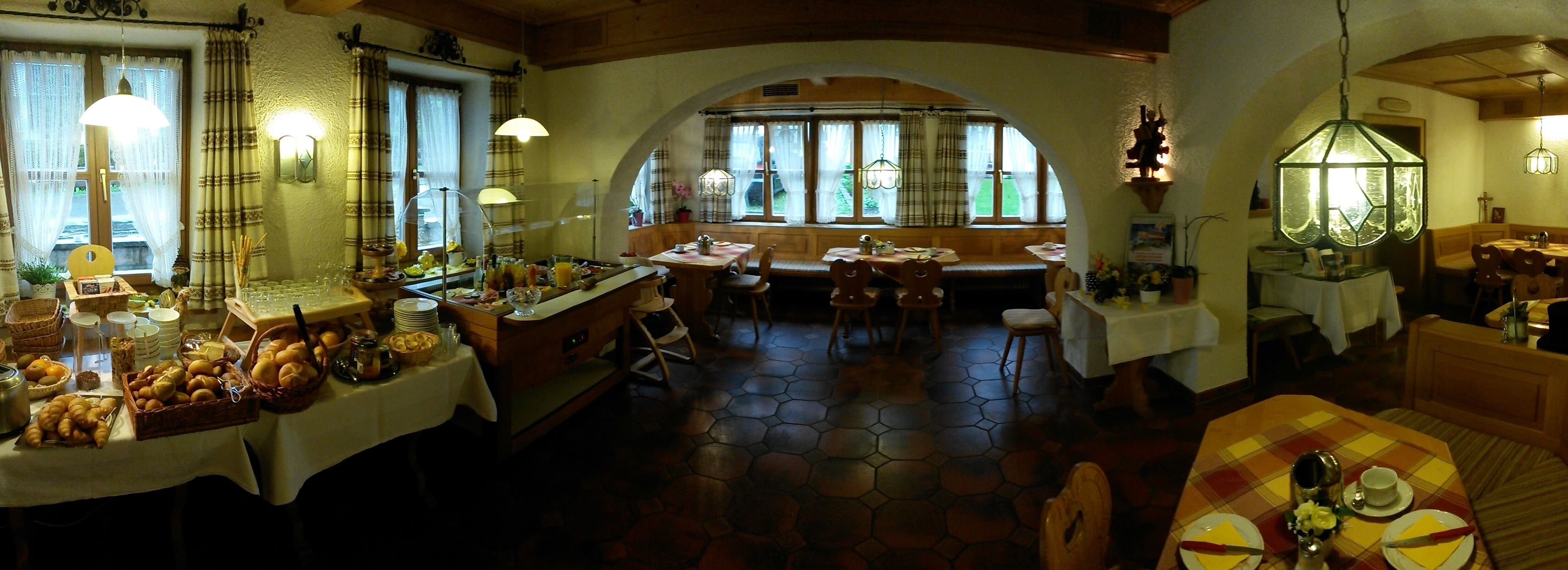 A cozy restaurant with hexagonal tiled flooring, wooden furniture, and a variety of food and drink items on tables.