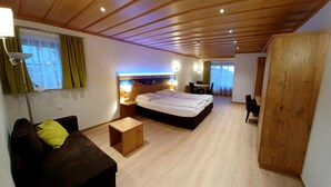 A modern hotel room with a wooden ceiling, a large bed, a small sofa, a desk, and a wardrobe. - Gästehaus Gritscher (Schliersee)