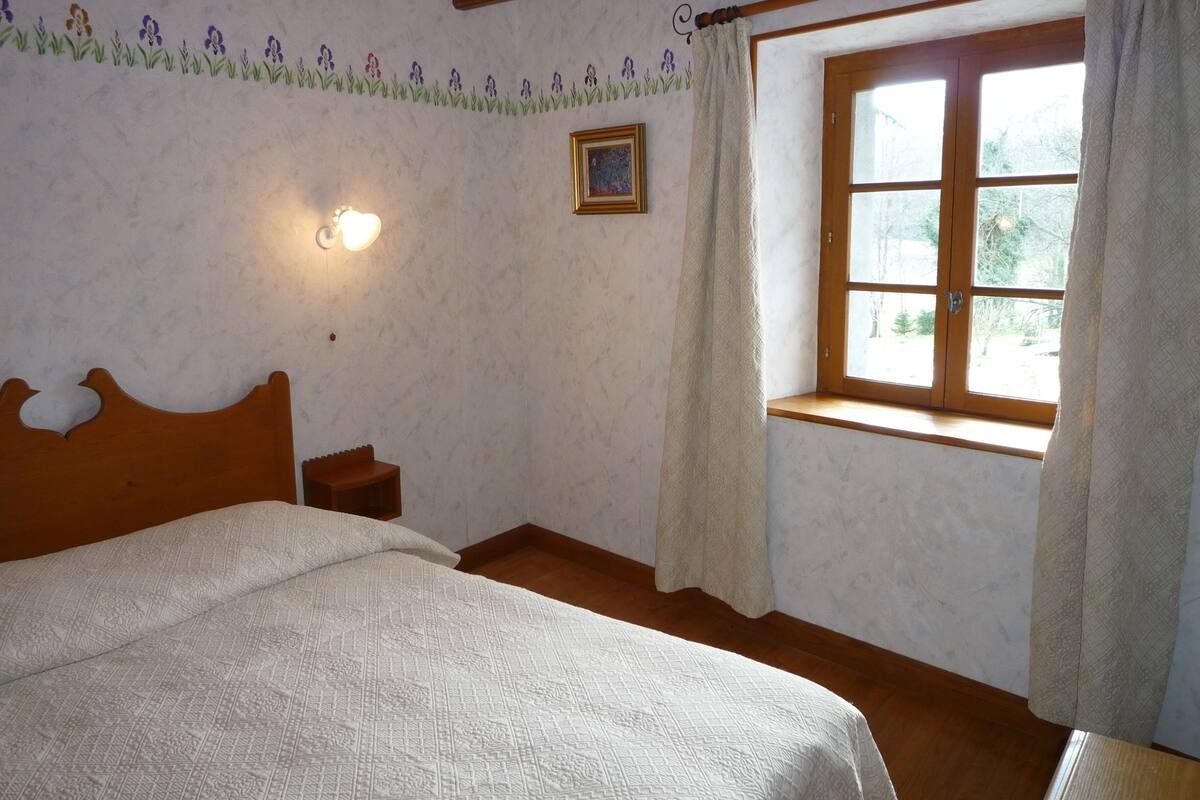 Un dormitorio con una cama de madera, una mesita de noche, una ventana con cortinas y un papel tapiz con motivos florales.