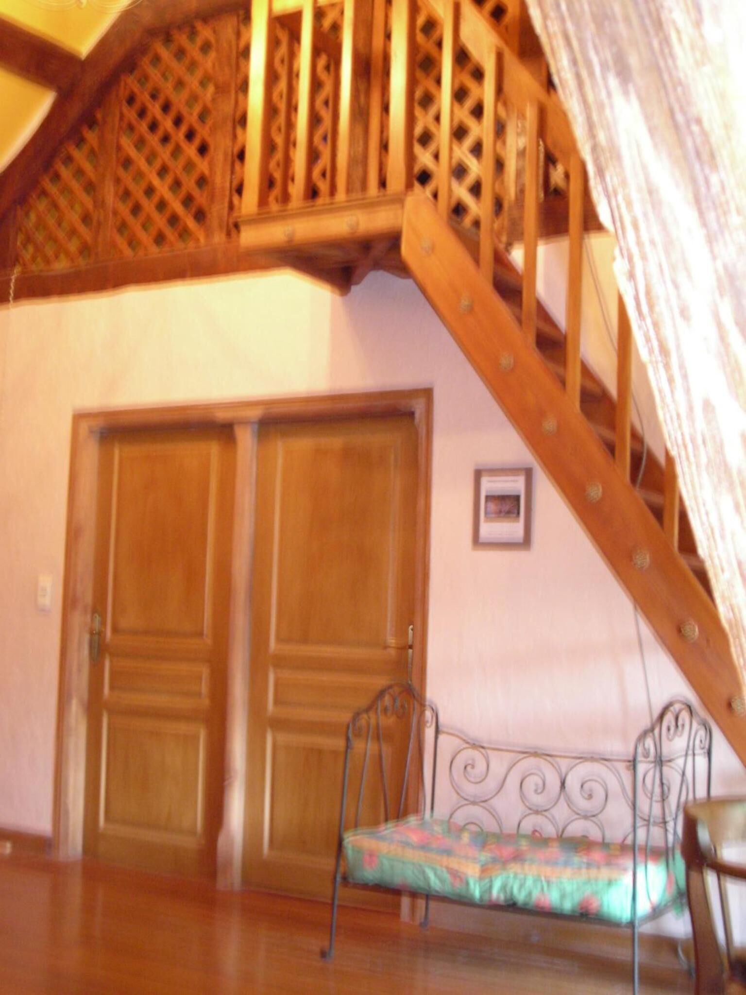 A room with a wooden staircase, two wooden doors, and a metal bed frame with a colorful cushion.