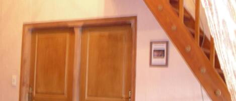 A room with a wooden staircase, two wooden doors, and a metal bed frame with a colorful cushion.