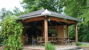 Ein hölzernes Pavillon mit Ziegeldach, Sitzgelegenheiten im Freien und einem steinbelagten Weg, der dorthin führt.