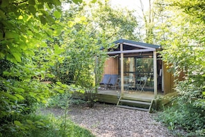 A wooden cabin with a glass enclosure, surrounded by dense greenery.