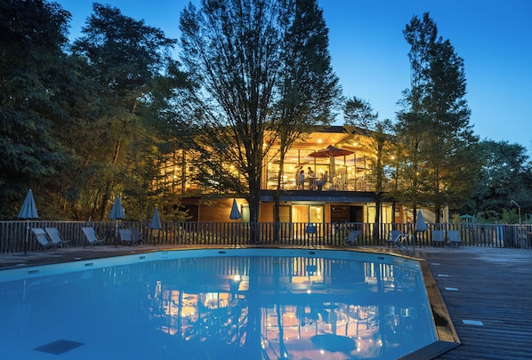 A swimming pool with lounge chairs and umbrellas, surrounded by a wooden deck and trees.
