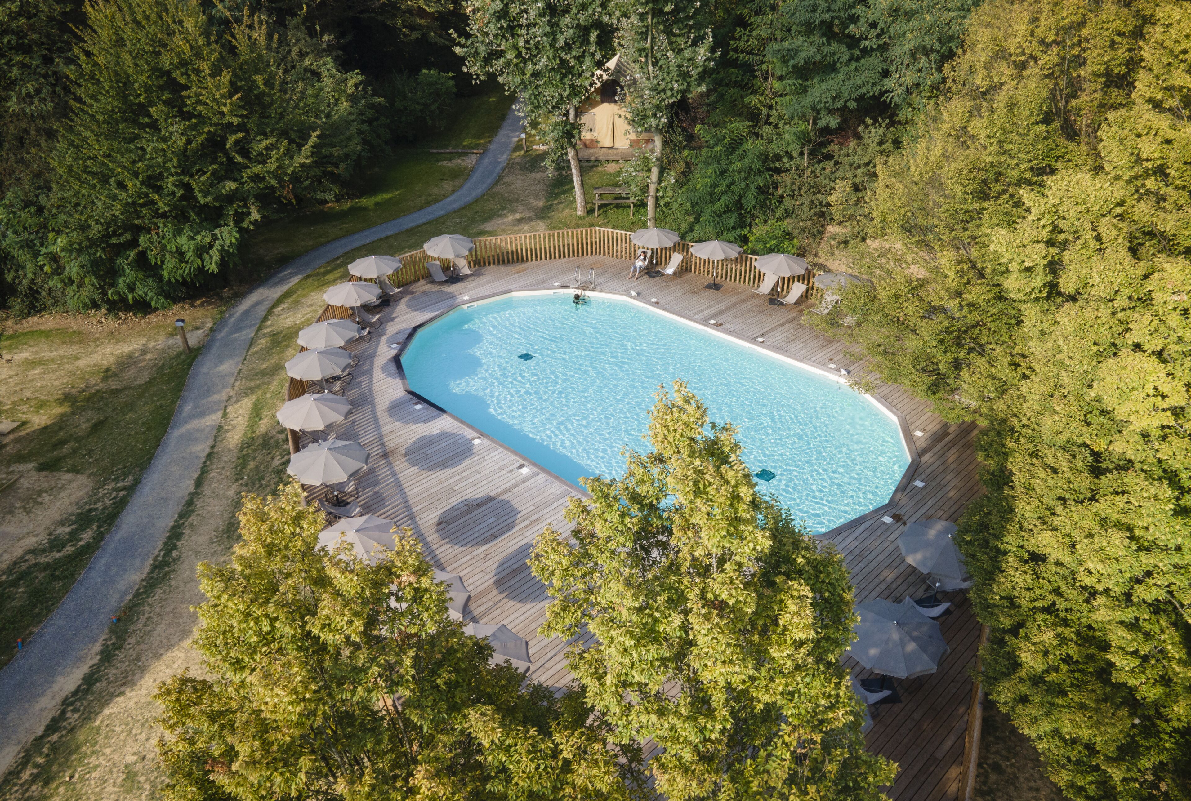 An aerial view of a rectangular swimming pool surrounded by a wooden deck with lounge chairs and umbrellas.
