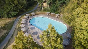 An aerial view of a rectangular swimming pool surrounded by a wooden deck with lounge chairs and umbrellas.