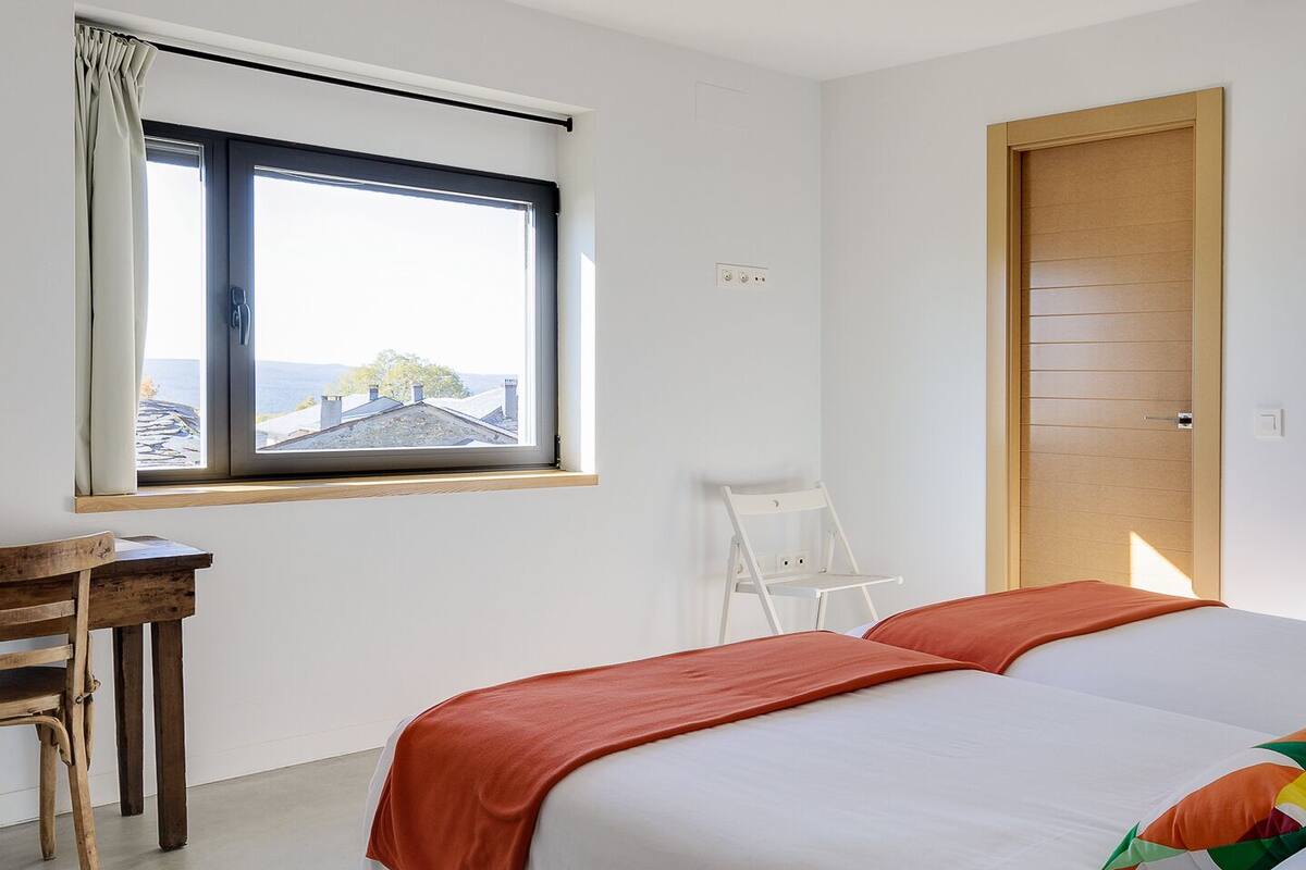 A modern bedroom with a large bed, a desk, and a window with a view.