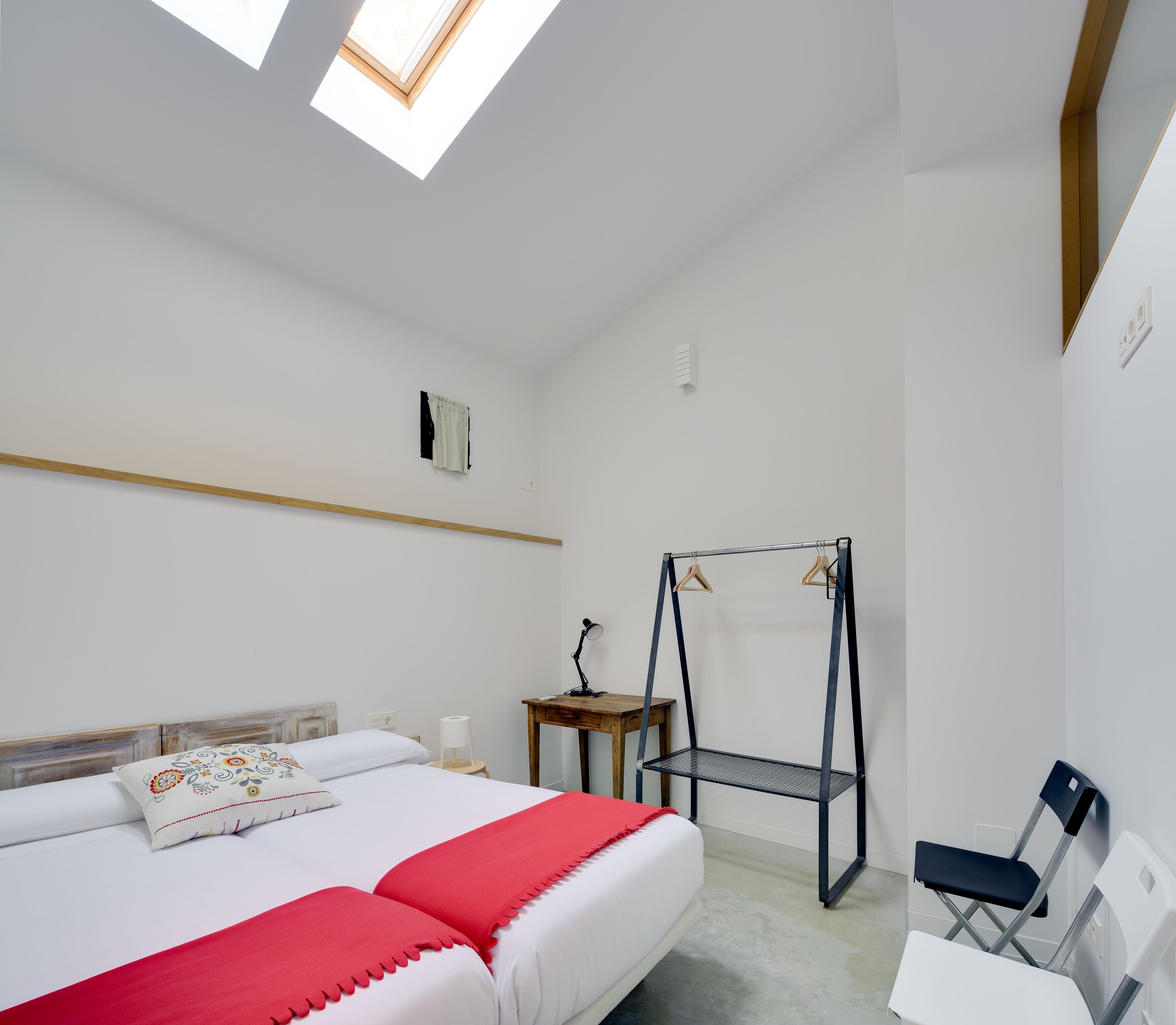 Ein Schlafzimmer mit Bett, einem kleinen Tisch, einem Sessel, einem Hängesessel und einem Dachfenster.