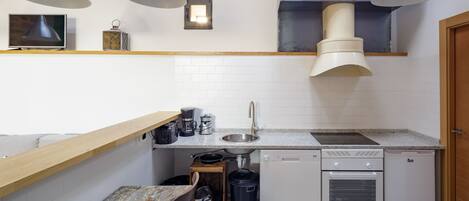 Una cocina compacta con encimera de madera, un fregadero, una estufa y un refrigerador. Hay luces en el techo y una ventana pequeña sobre el fregadero.