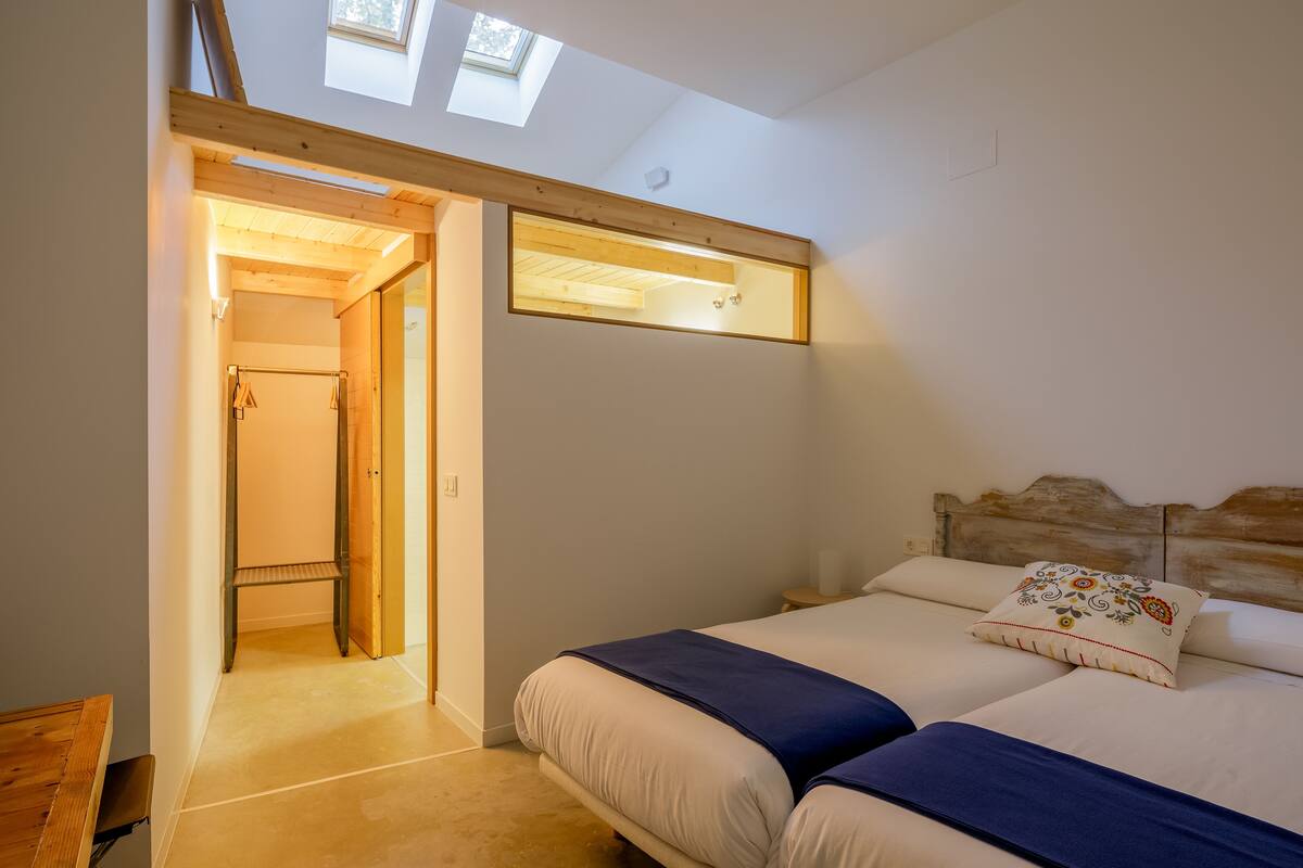 A bedroom with two beds, a skylight, and a wooden headboard.