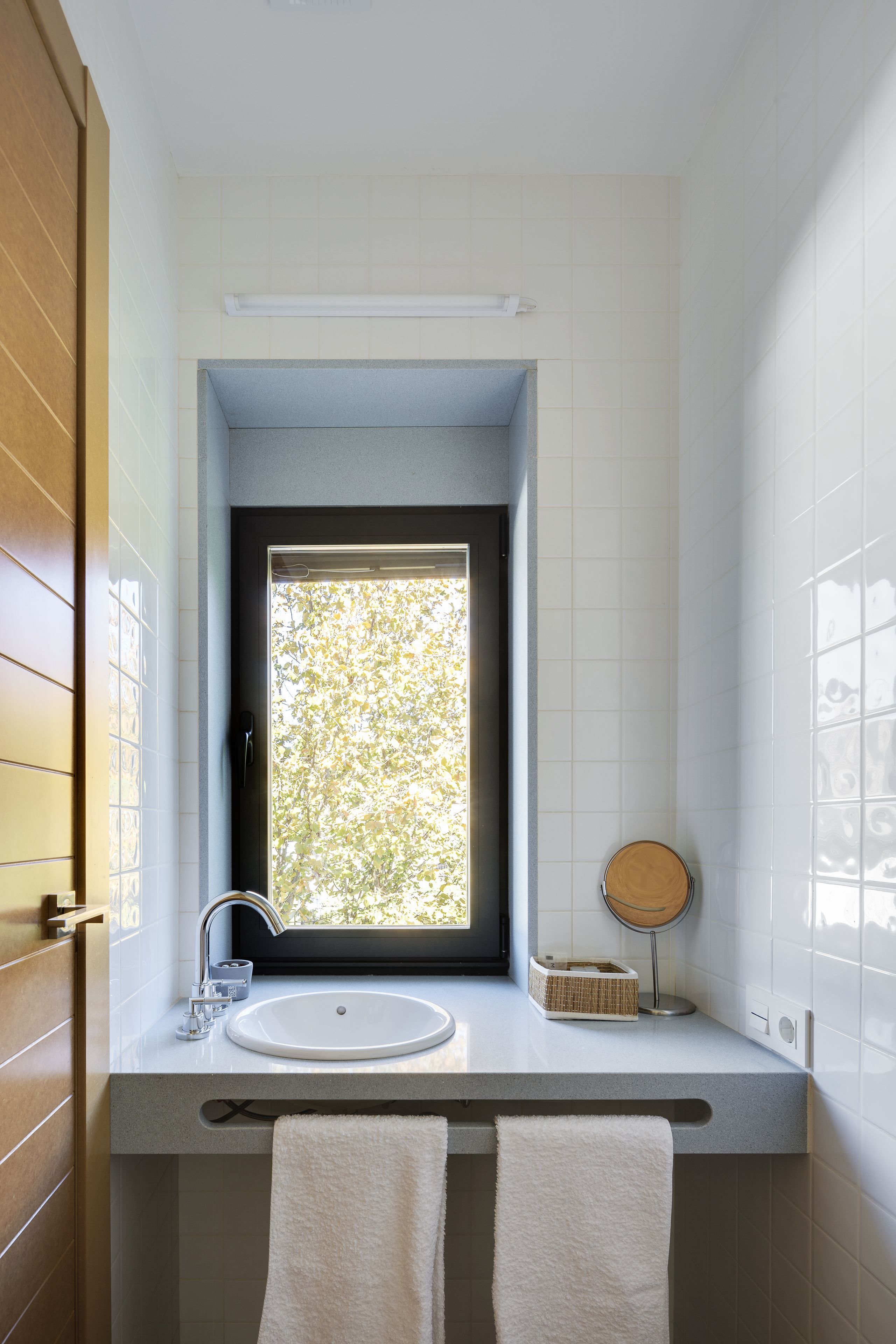 Un baño con ventana, un lavamanos, un espejo y dos toallas.