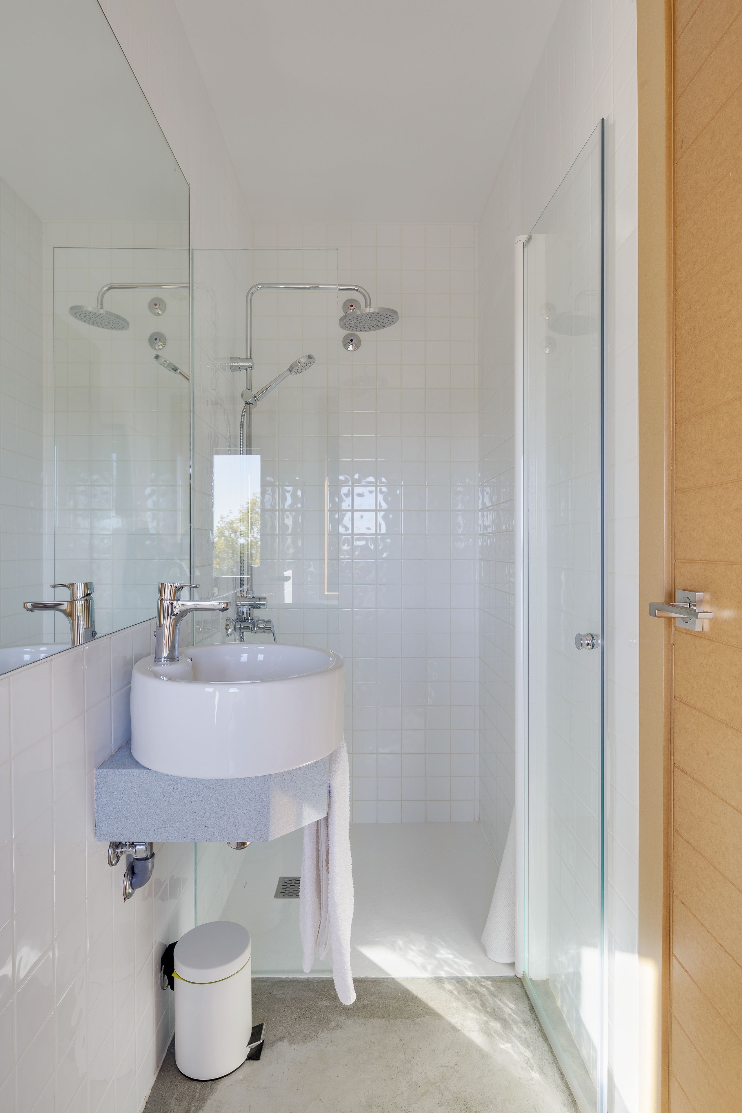 Un baño moderno con cabina de ducha de vidrio, lavabo blanco y puerta de madera.
