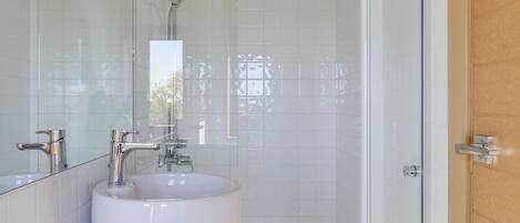 Un baño moderno con cabina de ducha de vidrio, lavabo blanco y puerta de madera.