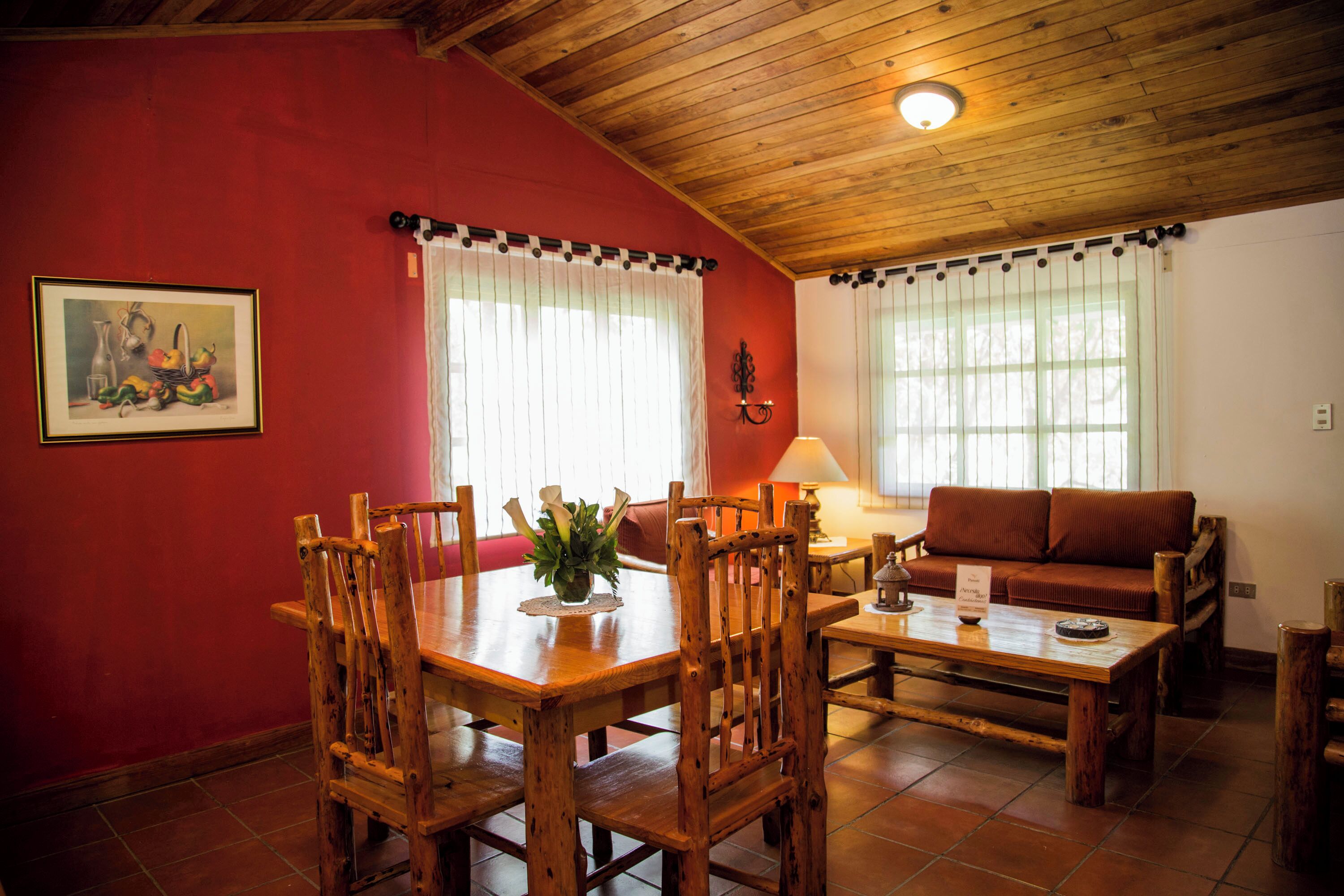 Un comedor con muebles de madera, pared roja y techo con vigas de madera.