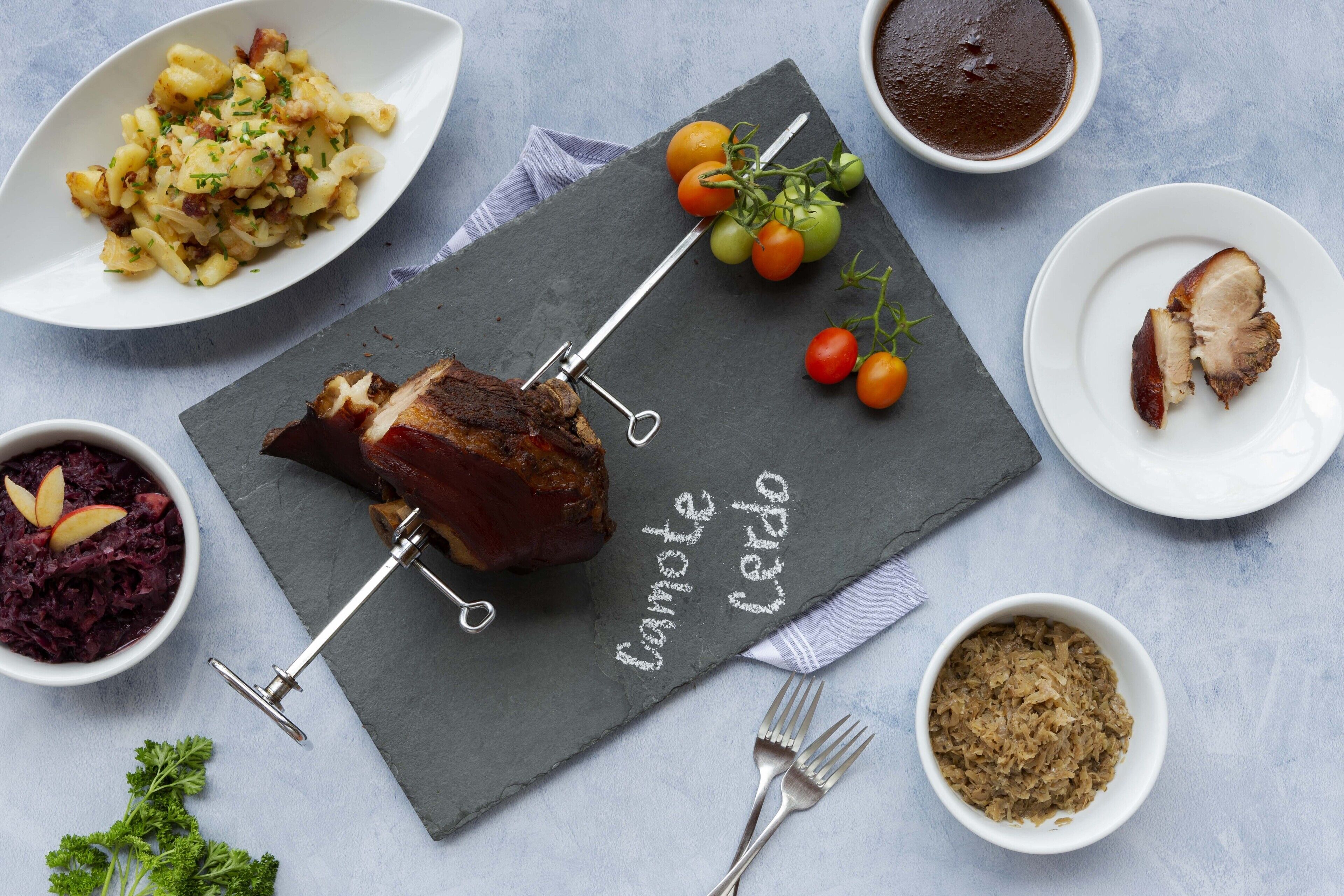 A meal with a roasted meat centerpiece, a side of potatoes, and a bowl of red cabbage.