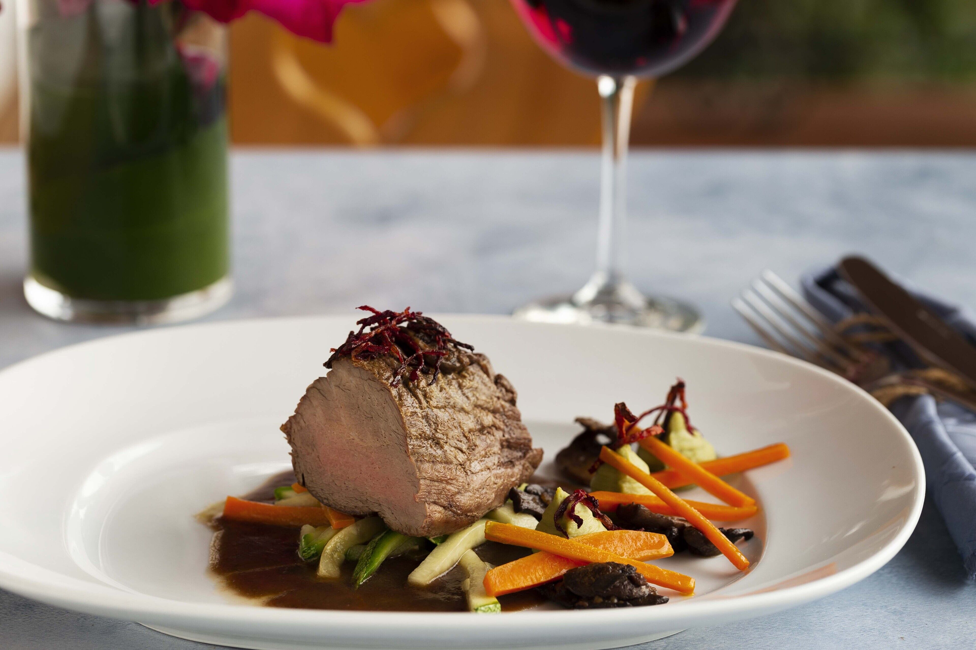 A plate of food with a large piece of meat, vegetables, and a glass of red wine.