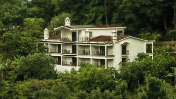 A multi-story building with balconies, surrounded by dense greenery.