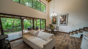 A spacious living area with a large window overlooking a lush garden, a sofa, a dining table with chairs, and a staircase. - Hotel Boutique Y Restaurante Panisté (San Cristobal Verapaz)