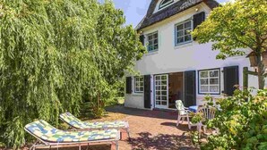 A two-story house with a thatched roof, a large tree in the foreground, and two lounge chairs in the backyard. - Holiday house Witte Hus (ID 175) - Holiday house "Witte Hus" (ID 175) (Sankt Peter-Ording)