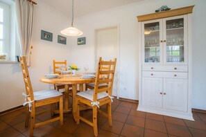 Un coin repas avec une table et des chaises en bois, un meuble avec des portes en verre et un luminaire suspendu.