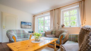 A cozy living room with two plaid sofas, a wooden coffee table, and a window with curtains. - Holiday house Witte Hus (ID 175) - Holiday house "Witte Hus" (ID 175) (Sankt Peter-Ording)