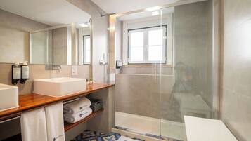 A modern bathroom with a wooden vanity, two sinks, a glass shower enclosure, and a patterned floor.