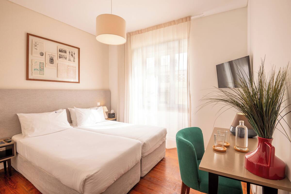 Una habitación de hotel con cama, mesita de noche, lámpara y televisión en la pared.