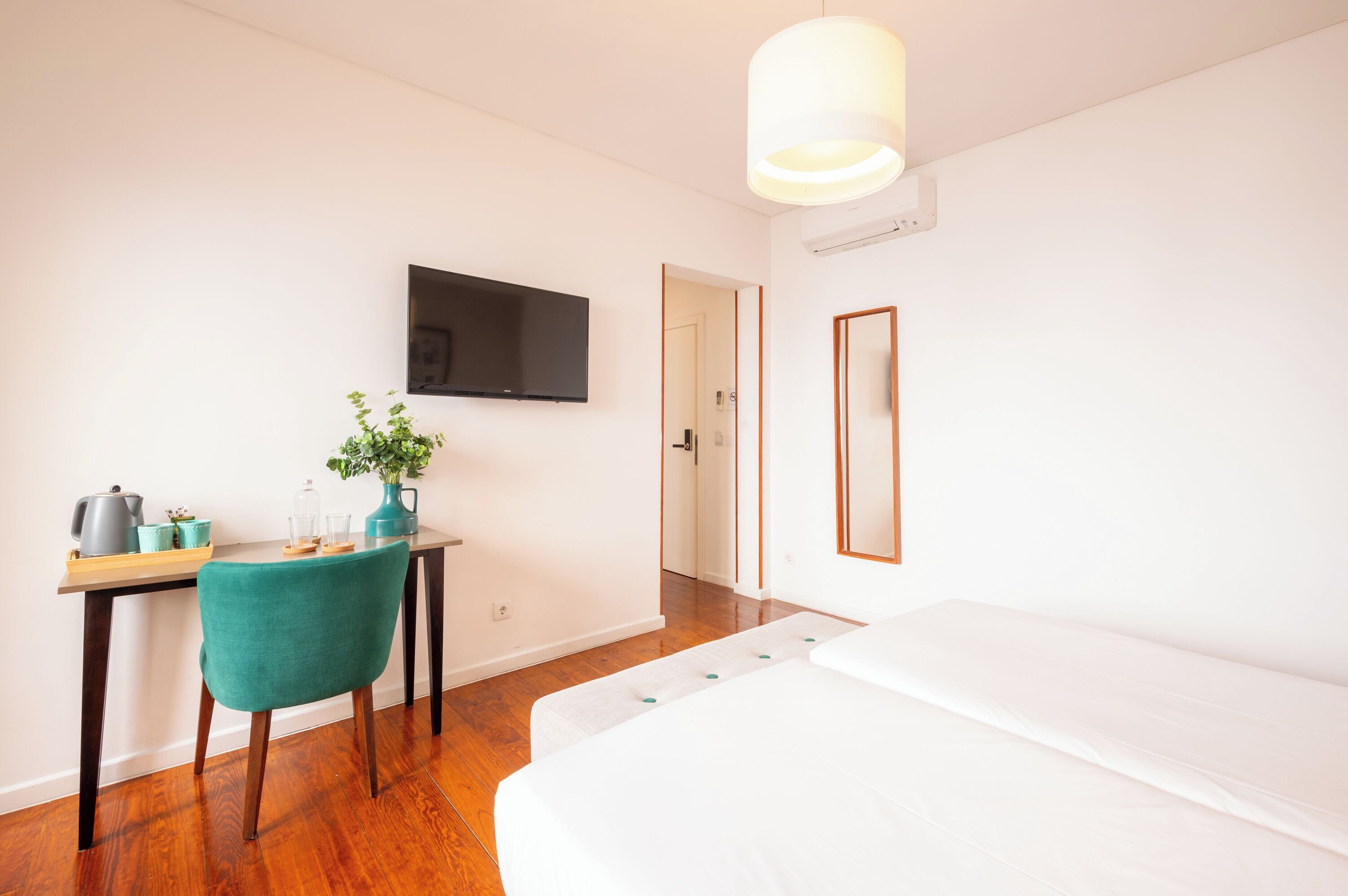 A room with a bed, a desk with a chair, a television, and a mirror.