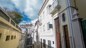 A narrow street with buildings on either side, a tram in the distance, and a clear sky. - Bica FLH Suites (Lisbon)