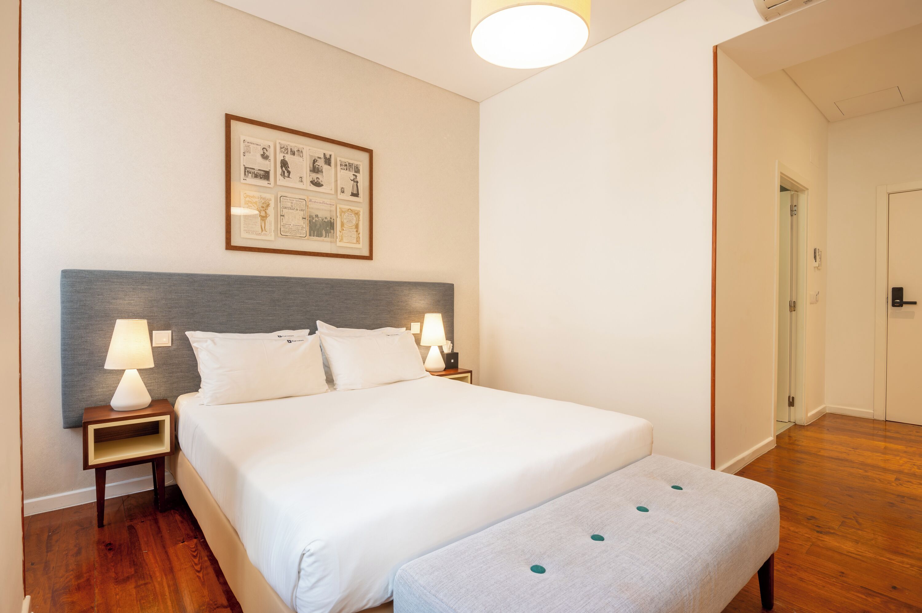 Une chambre d’hôtel bien aménagée, avec un grand lit, des lampes de chevet, un tableau encadré au mur et un plancher en bois.