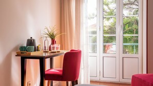 A room with a table set for two, a red chair, a bed, and a large window with a view of greenery outside. - Bica FLH Suites (Lisbon)