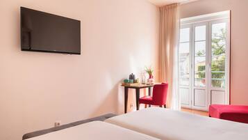 Een hotelkamer met een bed, een aan de muur bevestigde televisie, een klein tafeltje met een stoel, en uitzicht op de omgeving door een schuifglazen deur.