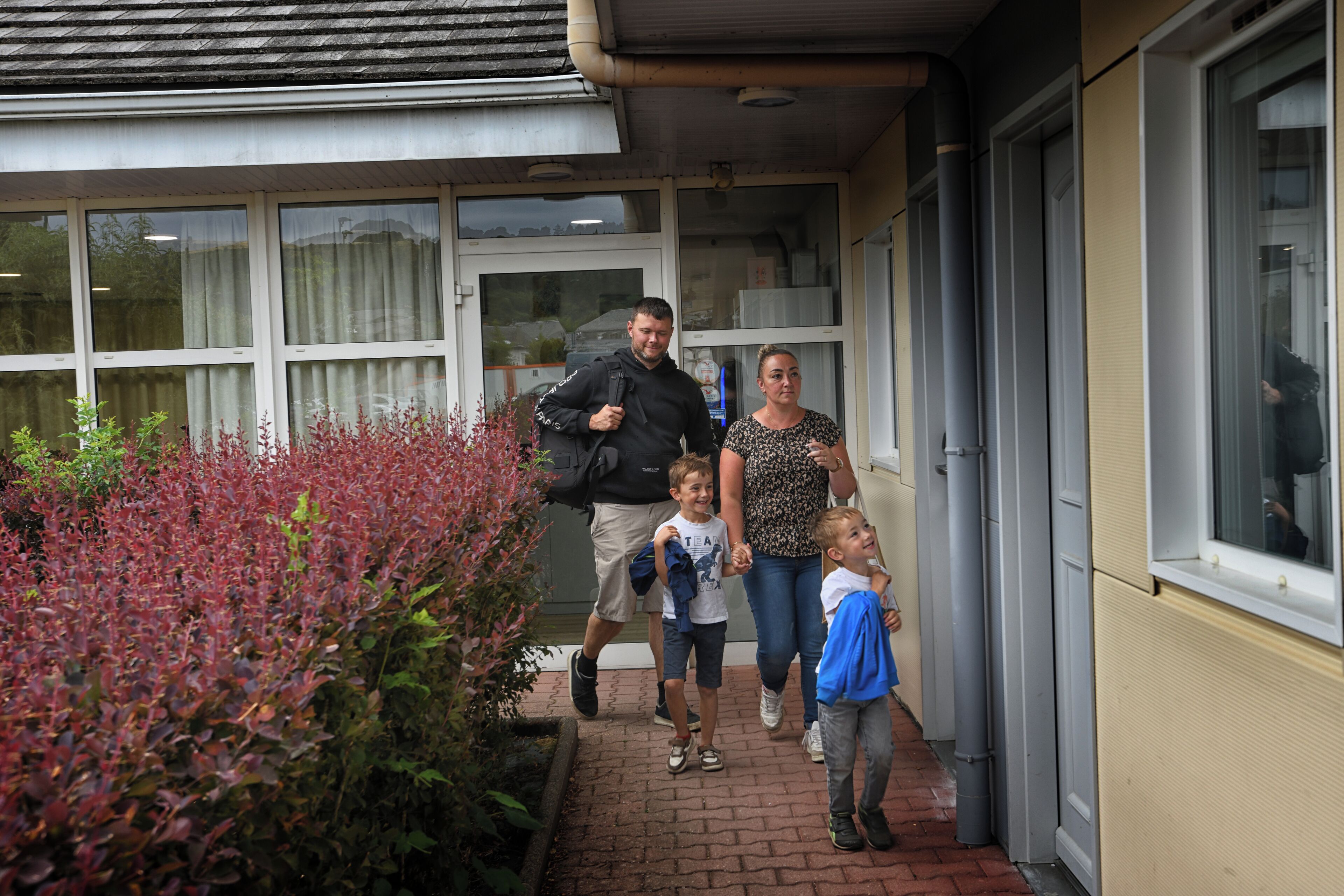 A family walking towards a building with large windows and a brick pathway.