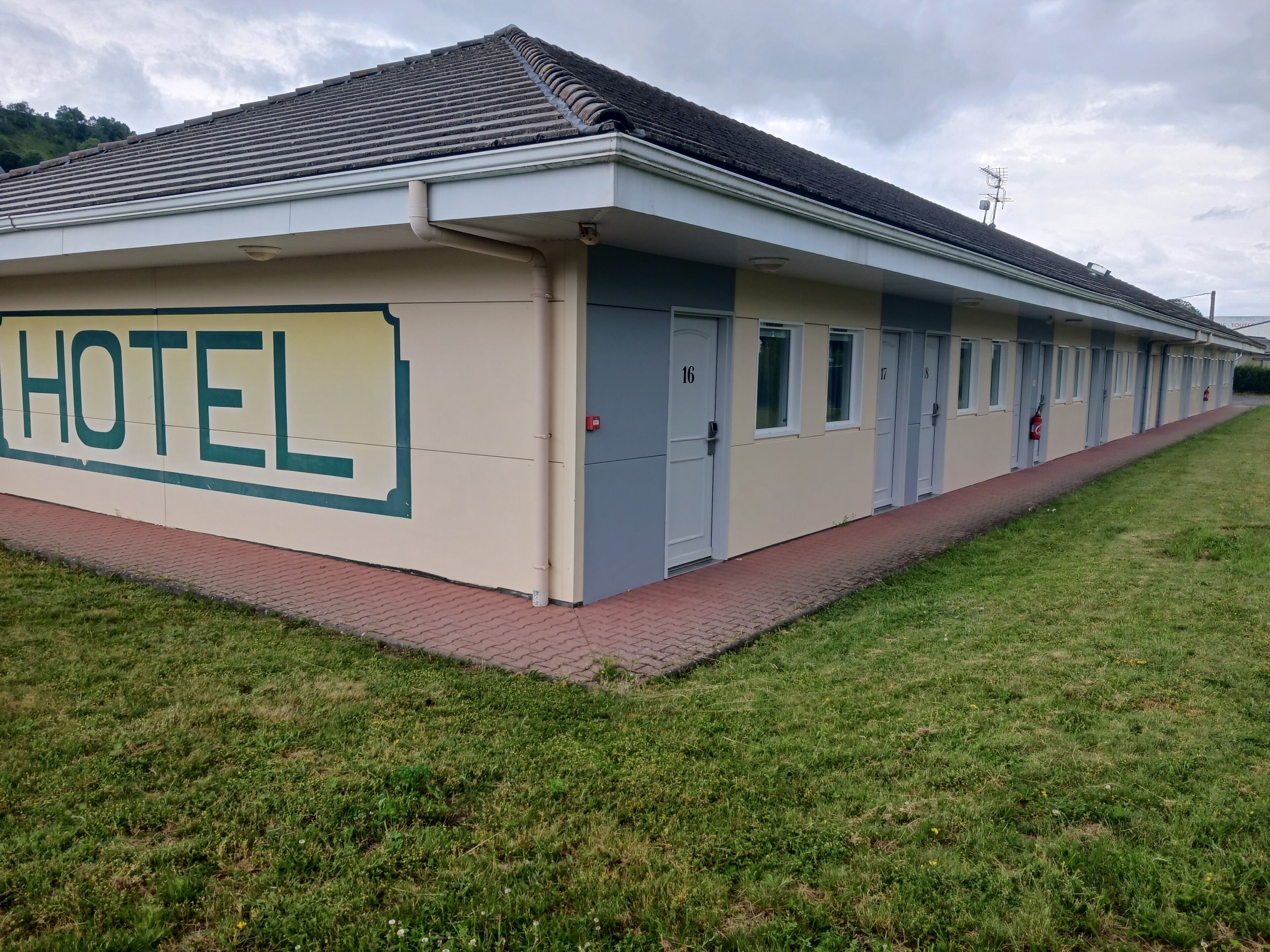 Ein Hotel mit flachem Dach, einer Beschilderung mit dem Schriftzug „HOTEL“ an der Seite und einem Ziegelweg, der zum Eingang führt.