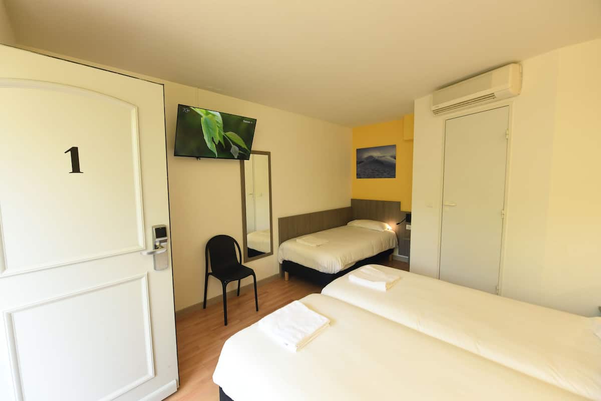 Ein Hotelzimmer mit zwei Betten, einem Fernseher, einem Spiegel, einem Sessel und einem Kleiderschrank.