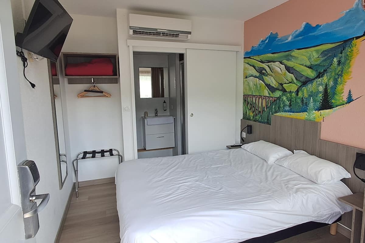 Ein Hotelzimmer mit Bett, Schreibtisch, Stuhl, Kleiderschrank, Spiegel und einem Bild an der Wand.