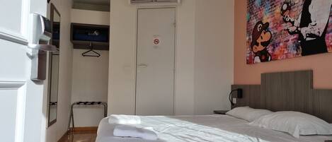 Una habitación de hotel con cama, televisión, puerta y un cuadro en la pared.