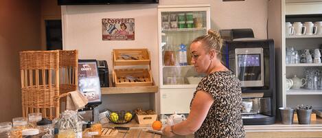 A coffee shop counter with a woman preparing a drink, a coffee machine, and various coffee-related items.