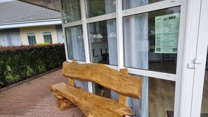 Un banc en bois se trouve devant un bâtiment doté de grandes fenêtres et d’une enseigne apposée sur l’une d’elles.