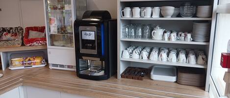 Una kitchenette con cafetera, refrigerador y estantes con vajilla y utensilios.