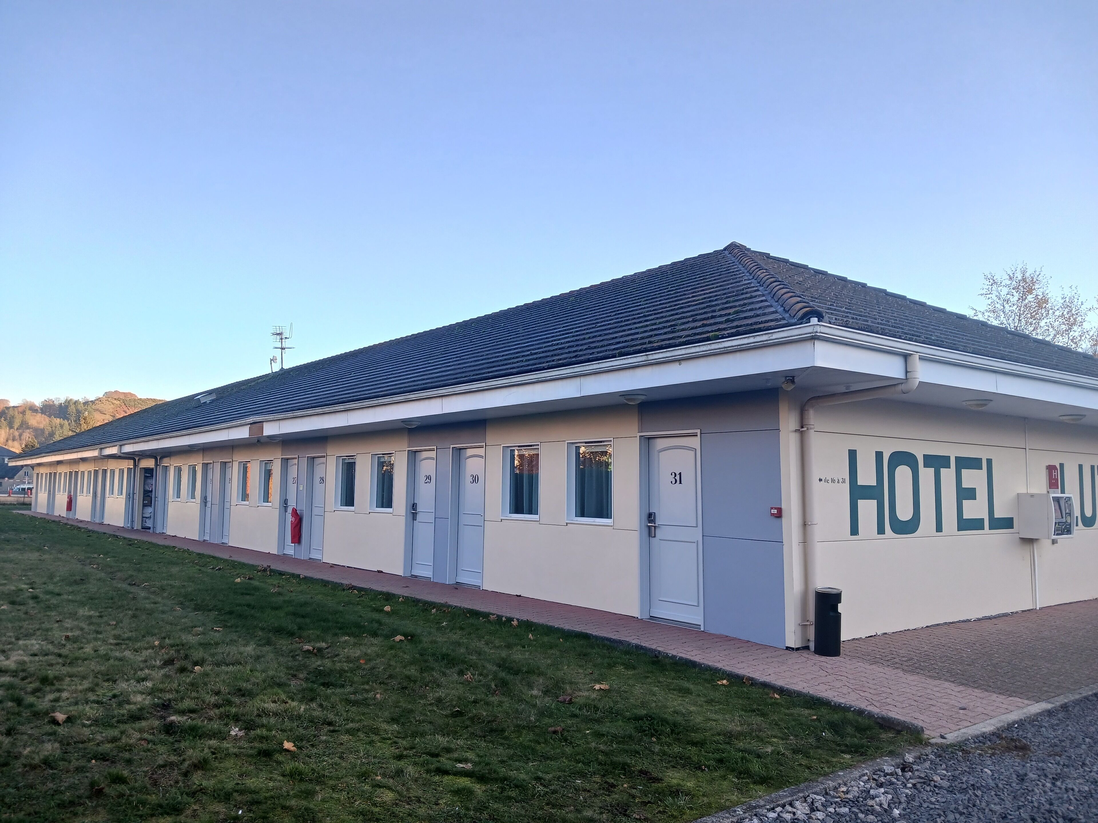 A hotel with a row of rooms numbered 25 to 31, a tiled roof, and a grassy area in front.